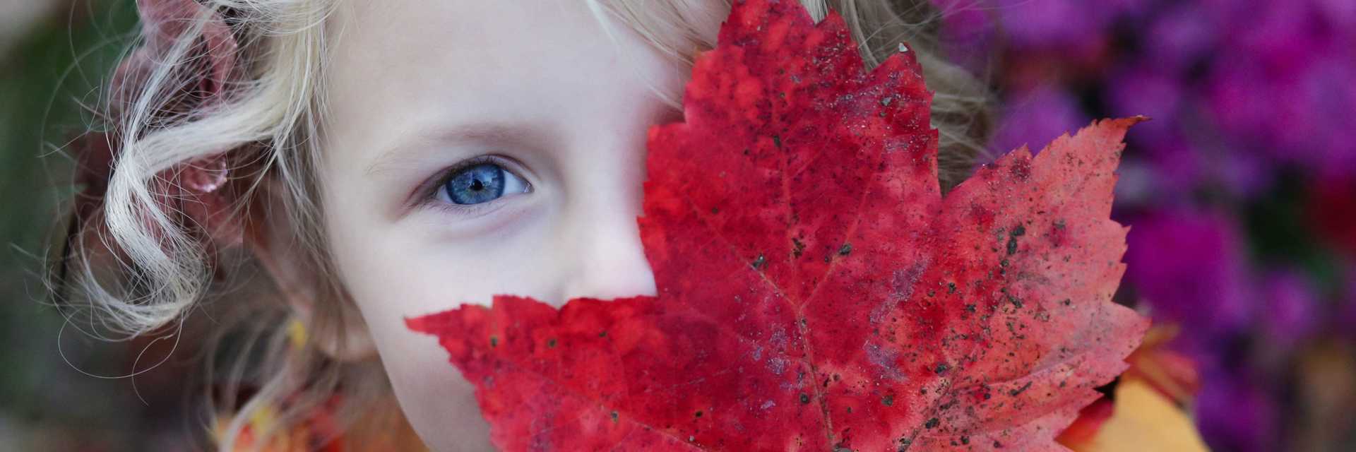 Efterår - barn står med et efterårsblad foran ansigtet